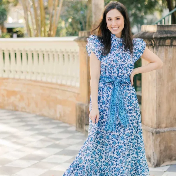 A woman in a blue floral dress smiling for a picture.